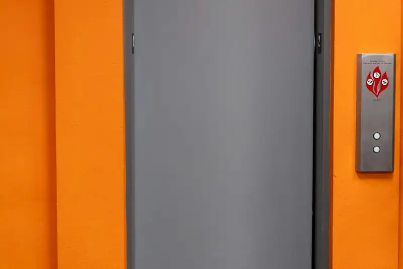 A closed grey lift door in an orange wall
